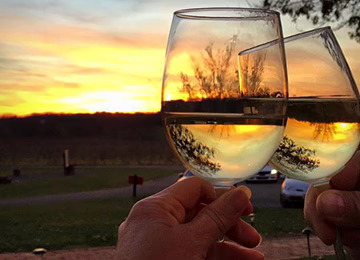 Two glasses of white wine clinking at sunset on the scenic grounds of Lansdowne Resort.