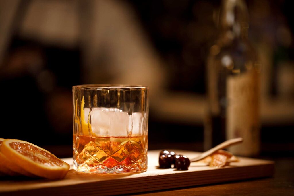 Whiskey cocktail with orange garnish and snack on a wooden tray