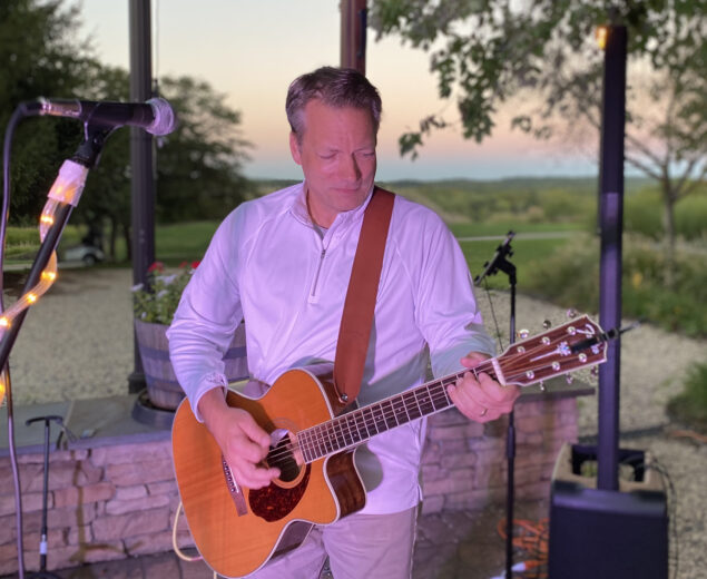 Live outdoor performance featuring Pete Leinbach playing an acoustic guitar.