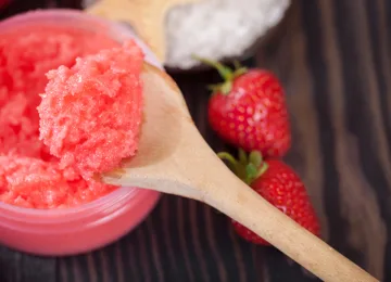 Spoonful of vibrant strawberry sugar scrub beside fresh strawberries