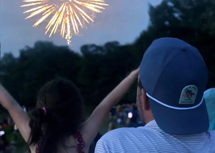 Back view of a guest in a cap watching colorful fireworks in the night sky
