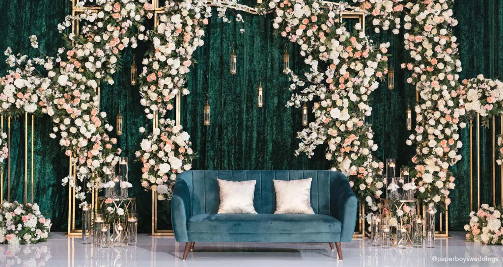 A floral backdrop behind a suede loveseat, set up for newlyweds after their wedding ceremony.