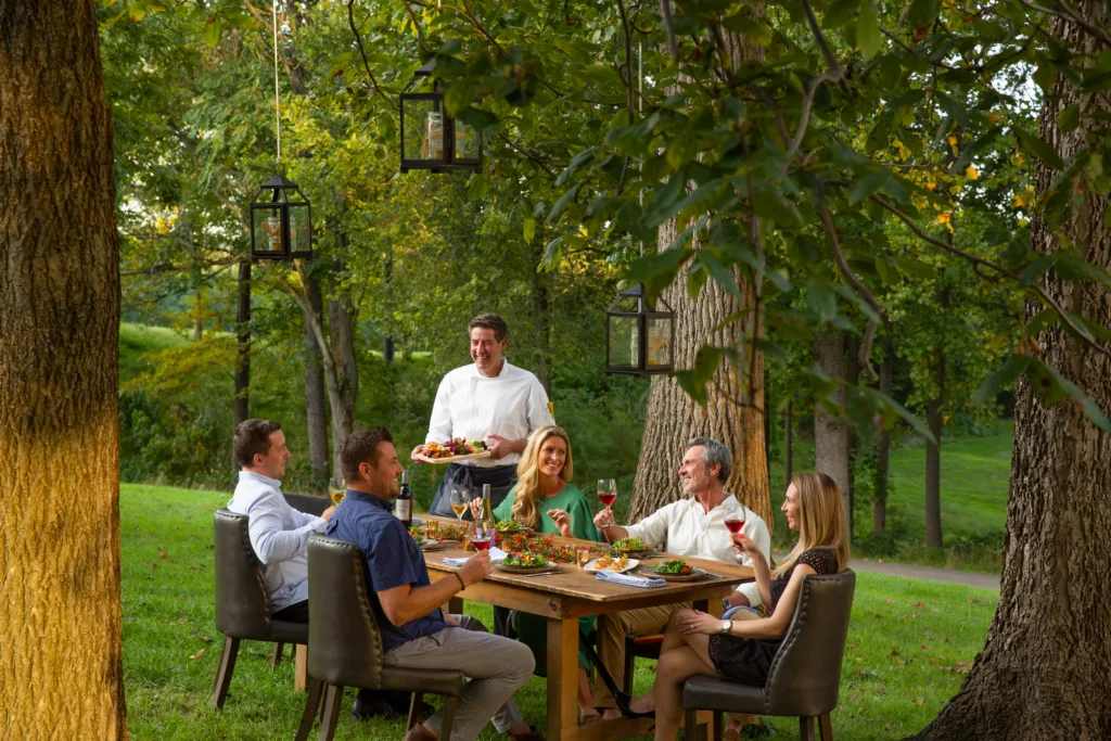 A group of people gathered at a wooden table outdoors at Lansdowne Resort, getting served a delicious platter of food.